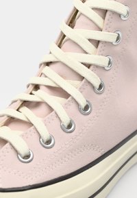 Rosa kanvas høyhælte sneakers med kremfargede snorer, sølvfargede øyer og svart gummisåle. Nærbilde viser teksturert materiale og søm detaljer.