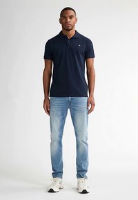 Granatowa koszulka polo z kołnierzykiem i logo, zestawiona z jasnoniebieskimi jeansami i białymi trampkami. Prosty fason z krótkim rękawem i prostym krojem.