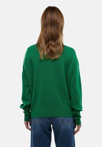 Pull vert ample en matériau doux, avec un ourlet et des manches côtelés, associé avec un jean bleu. Vue arrière simple.