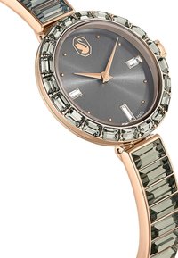 Okrągły zegarek z szarym cyferblatem, różowym złotem na akcentach oraz prostokątnymi zdobieniami z kryształu na obręczy i bransolecie. Posiada minimalistyczne znaczniki godzin.