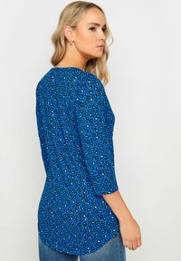 Sinine leopardimusteriga ülemine osa, millel on kolmandiku pikkused varrukad, ümmargune kaelus ja kõver hem. Valmistatud pehmest, tekstuursetest kangast.