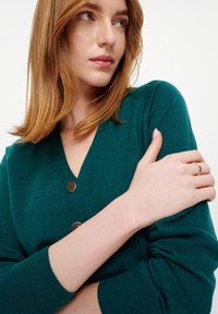 Cardigan lavorato a maglia color turchese con scollatura a V e tre bottoni metallici. La texture è morbida e con lavorazione a coste sulle maniche.
