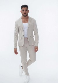 Blazer beige ajusté avec poches, accompagné d'un pantalon assorti. Un débardeur blanc en dessous et des baskets blanches complètent la tenue.