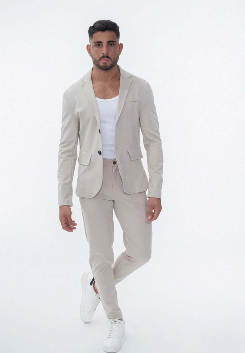 Blazer beige ajusté avec poches, accompagné d'un pantalon assorti. Un débardeur blanc en dessous et des baskets blanches complètent la tenue.