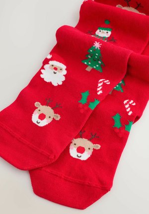 Red socks featuring white Santa, green Christmas tree, light brown reindeer with red nose, holly, and candy cane designs. Soft knit texture.