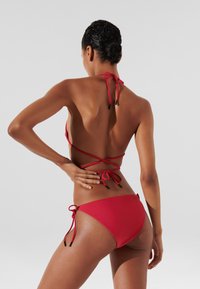 Rode bikini met een haltertop met kruislingse banden aan de achterkant en een low-rise broekje met zijbanden en zwarte accenten. Glad van textuur.