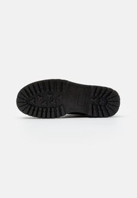 Suola di scarpa nera con modelli di battistrada profondi e un logo di marca rettangolare, fotografata su uno sfondo bianco.