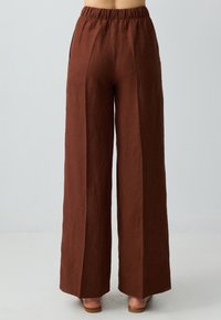 Pantaloni larghi in lino marrone con vita elastica, dotati di tasche laterali e una finitura testurizzata. Design svasato che si estende fino alla caviglia.