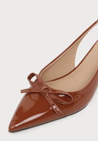 Γυαλιστερό καφέ παπούτσι slingback με μυτερή μύτη, με μια ταιριαστή λεπτομέρεια φιόγκου μπροστά και μπεζ εσωτερική επένδυση.