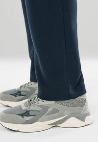 Grå sportsko lavet af en blanding af mesh og ruskind, parret med marineblå sweatpants, der er tapered ved bæltet, og har en blød tekstur.