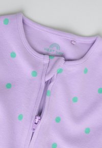 Vêtement bébé lavande avec des pois verts, encolure ronde et fermeture éclair centrale partiellement descendue.