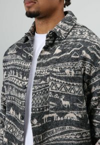 Grijs-wit geruit flannel overhemd met een kraag, voorzien van verschillende dieren- en geometrische patronen en zwarte knopen.