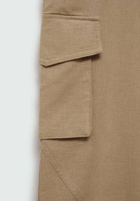 Beige cargozakdetail op gestructureerde stof. Kenmerkt een klepzak en stikselaccent. Het materiaal lijkt lichtgewicht en geweven.