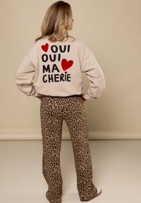 Beige sweatshirt met rode en zwarte letters op de rug met de tekst "Oui, ma chérie." Bruin luipaardprint wijde broek. Zachte textuur.