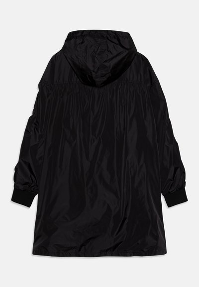 Black lightweight jacket with a hood, gathered detailing, and elasticized cuffs. Smooth, shiny finish with a relaxed fit and minimal design.