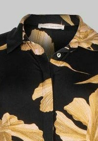 Czarna koszula z dużym złotym wzorem liścia. Posiada kołnierzyk i zapięcie na guziki z przodu. Wykonana z gładkiego materiału o miękkiej teksturze.