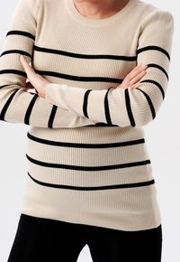 Beżowy sweter prążkowany z czarnymi poziomymi paskami, z okrąg�łym dekoltem i długimi rękawami, w połączeniu z czarnymi dopasowanymi spodniami.