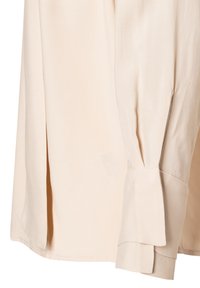 Langärmliges Shirt in hellbeige mit seitlichem Schlitz und gepufftem Ärmelabschluss, gefertigt aus einem glatten Material.