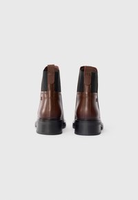 Brown leather ankle boots with black elastic side panels, pull tabs, and a sturdy black rubber sole. Smooth texture with minimal detailing.