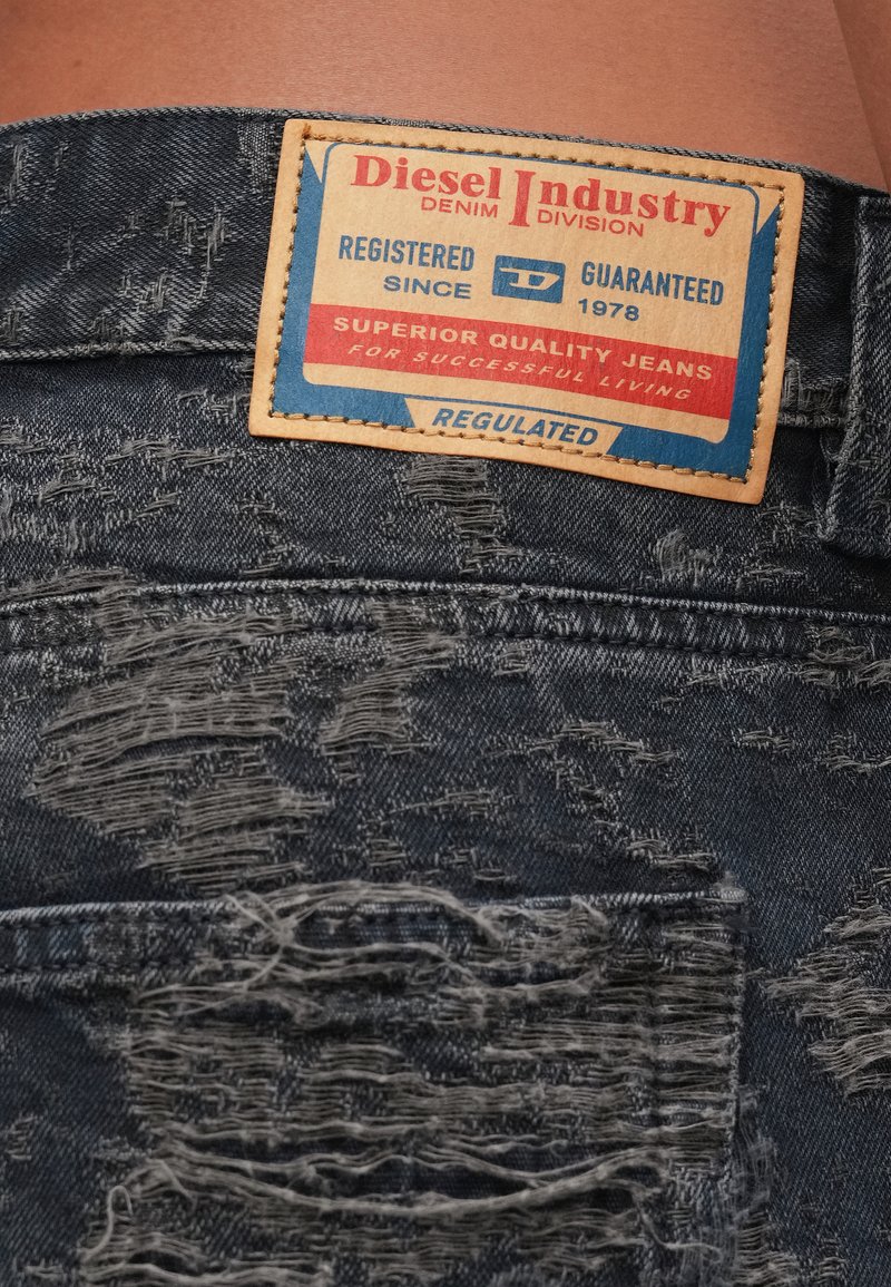Abgenutzte, dunkle Jeans aus Denim mit einem getragenen Lederpatch, auf dem "Diesel Industry Denim Division" und Markendetails stehen.