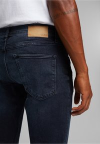 Mörkblå denimjeans med ett beige lädermärke på midjan och två bakfickor med subtila sömdetaljer.