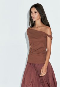 Top marrone a spalle scoperte con dettagli arricciati, abbinato a una gonna fluida color bordeaux. Tessuto morbido e silhouette rilassata.
