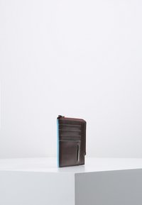 Cartera de cuero marrón con un acento azul, que cuenta con múltiples ranuras para tarjetas, un compartimento con cremallera y una textura suave.