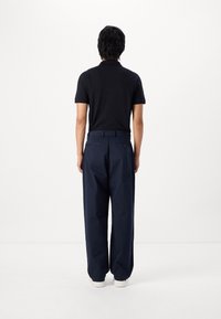 Black polo shirt with short sleeves, paired with loose-fitting navy trousers and white sneakers, viewed from the back.