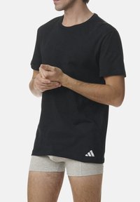 Black cotton t-shirt with short sleeves and a crew neck; features a white logo on the lower left. Gray shorts underneath.