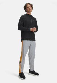 Men's athletic outfit featuring a black zippered jacket and light gray pants with orange stripes. Made of lightweight, breathable material.