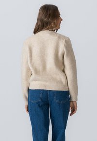 Cremefarvet strikket sweater med rund halsudskæring og ribbet kant, parret med blå jeans med høj talje og baglommer.
