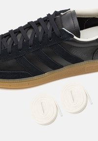 Czarne skórzane i zamszowe sneakersy z trzema ciemnymi paskami, białymi sznurowadłami i gumową podeszwą. W zestawie znajdują się dwa dodatkowe białe sznurowadła.