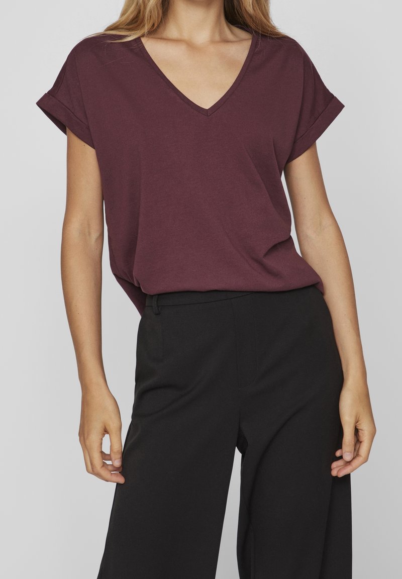 Burgunderfarbenes V-Neck-T-Shirt mit kurzen aufgerollten Ärmeln, aus weichem Stoff, kombiniert mit schwarzen weit geschnittenen Hosen; lässiger Schnitt.