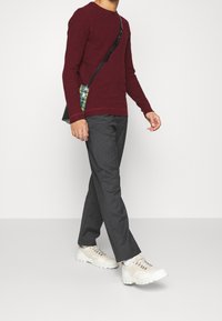 Bordowa koszula z długim rękawem, szare spodnie, białe trampki z teksturowanymi detalami. Czarna torebka na ramię z wielokolorowymi akcentami.