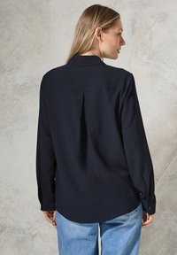 Marineblauw geweven shirt met een relaxed fit, rugplooidetail, lange mouwen en knoopmanchetten, gecombineerd met lichtblauwe denim jeans.