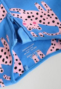 Blå stof med et legende mønster af pink leoparder og sorte pletter. Har lynlås og blød tekstur. Etiket synlig nær sømmet.