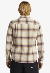 Camisa de cuadros en crema, naranja y azul. Tejido suave con mangas largas, puños con botones y detalle en la parte trasera.