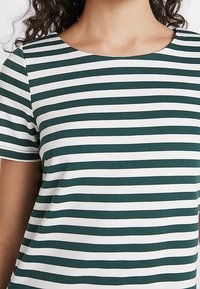 Zeleno-bílý pruhovaný krátký rukáv s kulatým výstřihem; vyrobeno z měkké tkaniny s hladkou texturou.