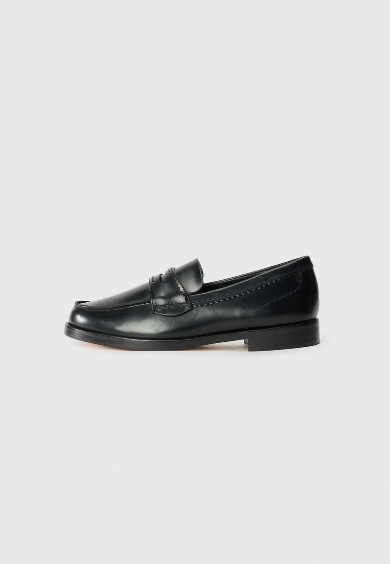 Black leather moccasin shoe with a rounded toe, raised stitching details, and a low heel. Smooth texture with minimal embellishments.