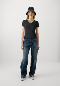Svart kortermet topp med V-hals og rynkedetalj, kombinert med slitte blå jeans og svarte joggesko med hvite såler.