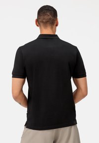 Polo shirt nera con colletto classico, maniche corte e una texture liscia. Presenta un orlo spaccato e una sottile branding sul lato.