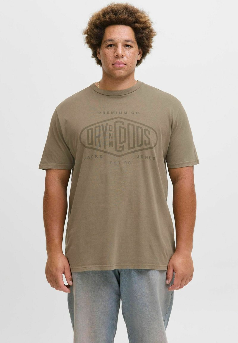 Olivengrøn T-shirt med korte ærmer og trykt logo i en mørkere grøn, parret med lyseblå denimjeans. Blødt bomuldsstof.
