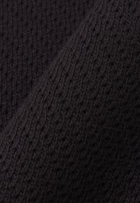 Primer plano de tela negra tejida que muestra bucles de hilo entrelazados y texturizados con patrón de puntadas visible.