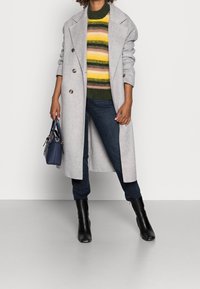 Szary wełniany płaszcz dwurzędowy nałożony na sweter w kolorowe paski, ciemne dżinsy i czarne botki za kostkę. W zestawie torebka w kolorze granatowym.