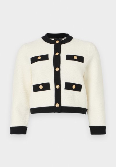 Ivory cropped cardigan in a textured knit, featuring black trim, two front pockets with black flaps, and gold buttons along the front.