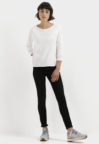 Witte lange mouwen shirt met een ronde hals, gecombineerd met slim-fit zwarte jeans en lichtgrijze sneakers met oranje accenten.