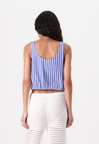 Modrý a bílý pruhovaný crop top s kulatým výstřihem a otevřeným zadním dílem. V kombinaci s bílými pletenými širokými kalhotami s texturou.