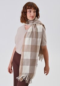 Beige en crème geruite sjaal van zacht stof, met franjes aan de randen. Het ontwerp bevat afwisselend grote vierkanten in kleur.