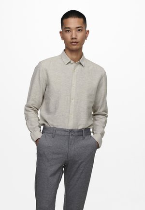 Camisa de botones de manga larga beige claro con cuello, combinada con pantalones gris oscuro a medida con cierre de botón y una sutil textura.