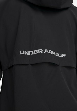 Zwarte sportjack met capuchon, gemaakt van gestructureerde stof, met zilveren "UNDER ARMOUR" branding langs de achterkant.